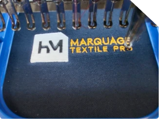 Logo HM Marquage Textile Pro brodé en gros plan sur textile bleu marine